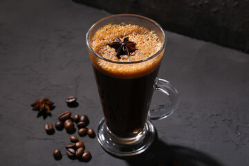 Glass of delicious espresso with star anise and coffee beans on dark background, closeup