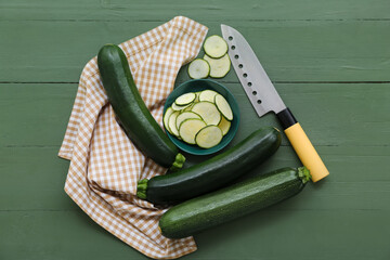 Fresh zucchini and bowl with slices on green wooden background