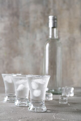 Shots and bottle of vodka with ice cubes on grey background