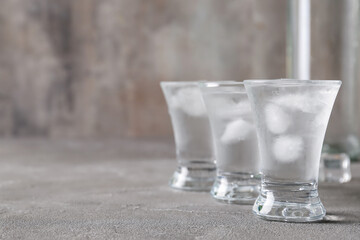 Shots and bottle of vodka with ice cubes on grey background