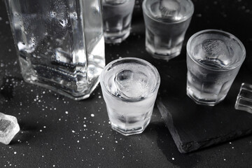 Shots and bottle of vodka with ice cubes on black background