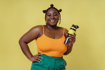 Fototapeta na wymiar Portrait of positive smiling African woman holding bottle of water isolated on yellow background. Concept of health care, healthy lifestyle, diet