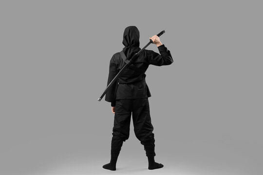 Male ninja with sword on grey background, back view