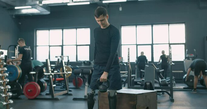 disabled sportsman with artifical legs raising kettlebell, working out with sport equipment, tool, strength health care.never give up Slow motion cross fit. endurance, willpower