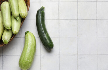 Wicker basket with fresh zucchini on white tile background