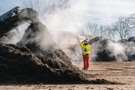 Woman worker standing with clipboard in industrial compost plant