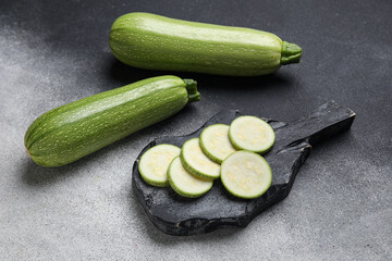 Board with slices of fresh green zucchini on grey background