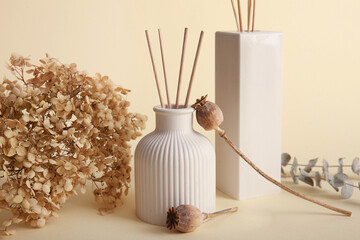 Bottles of reed diffuser, dry poppy heads and hydrangea flowers on beige background, closeup