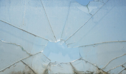 Cracks in the window glass on a background of blue sky. Broken glass, backdrop of cracked window against blue sky