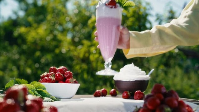Female hand taking strawberry milkshake cocktail with straw on nature backdrop