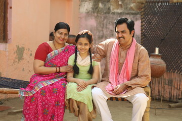 Happy rural Indian family sitting together outside their cottage in a village.