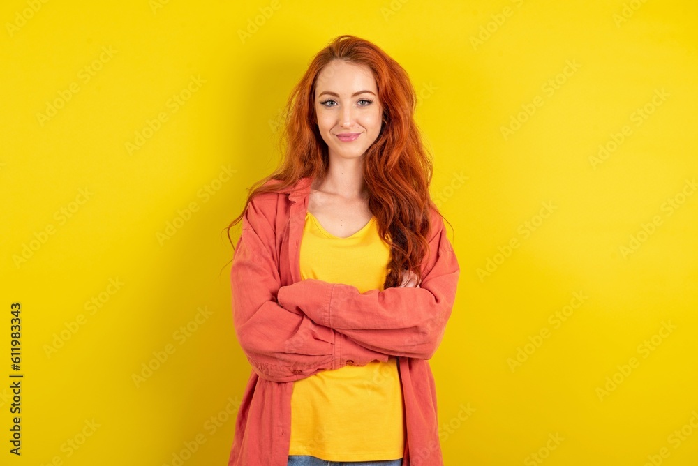 Wall mural Dreamy rest relaxed young beautiful red haired woman over yellow studio background crossing arms,