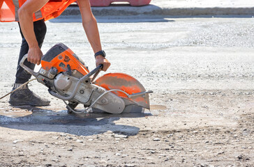 A petrol disc cutter in the hands of a worker cuts the asphalt concrete road surface on a sunny summer day. - 611984744