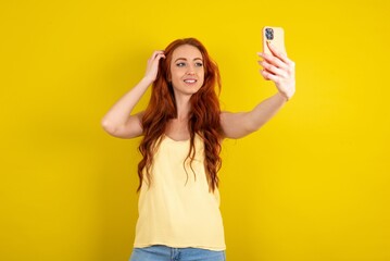 young beautiful red haired woman wearing yellow blouse over yellow studio background smiling and...
