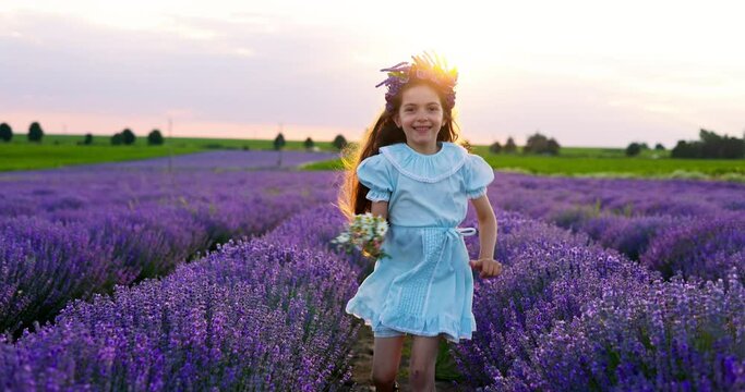 Happy carefree little girl with beautiful dress running in lavender field rows at sunset