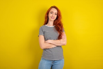 Portrait of charming young beautiful red haired woman wearing striped shirt over yellow studio...