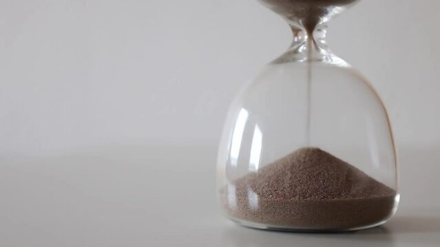 Sand goes through the bulbs of an hourglass on a white background