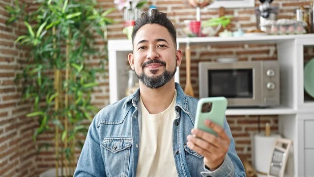 Young latin man using smartphone saying yes with head at dinning room