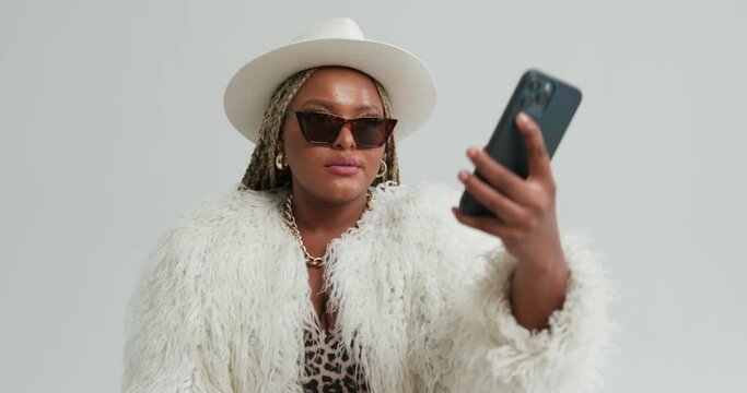 plump stylish smiling African Woman in sunglasses hat fur coat leopard dress making taking selfie isolated over white background. American rich business woman using gadget Slow motion fashion