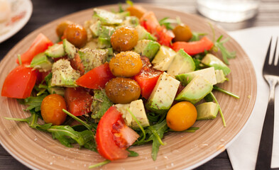 dish of fresh vegetables arugula, avocado, cherry tomatoes with olives on dining table