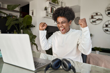 Excited African American student celebrating online win screaming looking at laptop. Happy gen z...