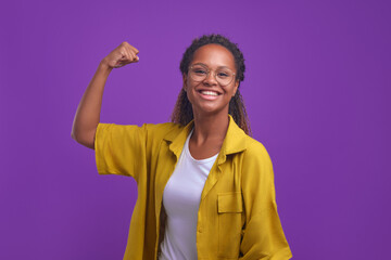 Young cheerful pretty African American woman laughs sincerely and demonstrates biceps on arm to...