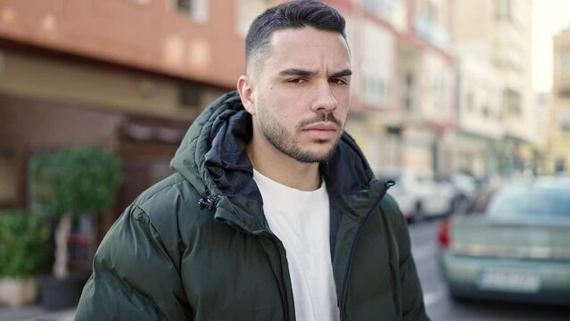 Young hispanic man standing with serious expression walking away at coffee shop terrace