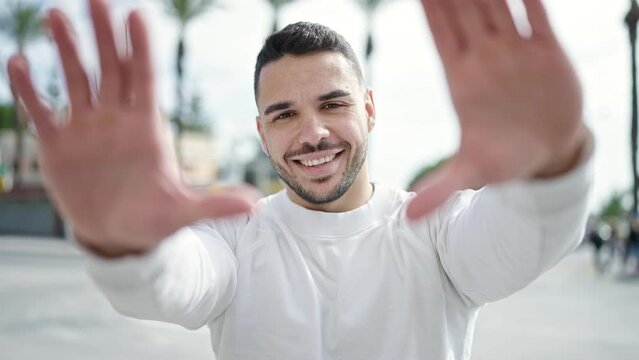 Young hispanic man smiling confident doing frame gesture with hands at street