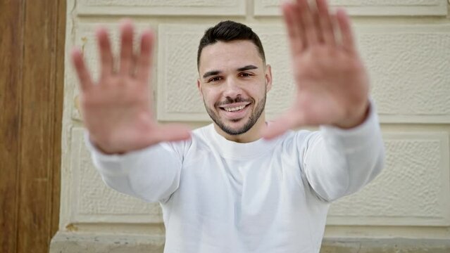 Young hispanic man smiling confident doing frame gesture with hands at street