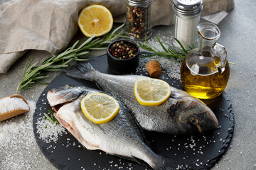Fresh sea bream fish with lemon, rosemary, olive oil and spices on a slate board, close up