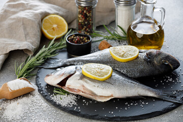 Fresh sea bream fish with lemon, rosemary, olive oil and spices on a slate board, close up