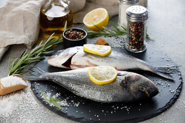 Fresh sea bream fish with lemon, rosemary, olive oil and spices on a slate board, close up