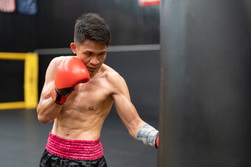 Asian boxer athlete man with red boxing glove training by punching to sandbag at the gym