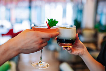 hands of man and women holding and clinking glasses cocktails in restaurant