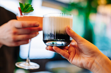 hands of man and women holding and clinking glasses cocktails in restaurant