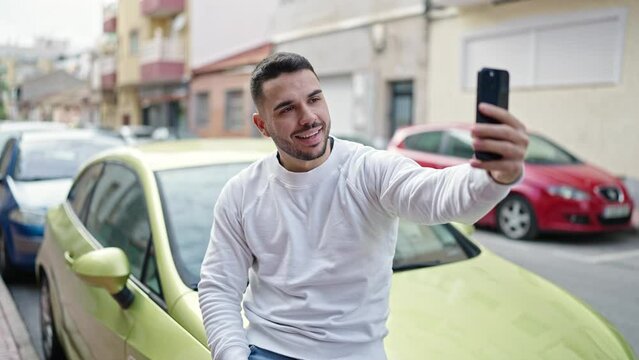Young hispanic man make selfie by smartphone pointing to car at street