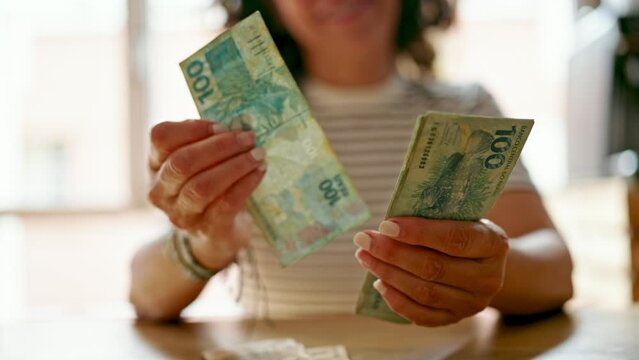 Middle age hispanic woman counting brazil real banknotes at the kitchen