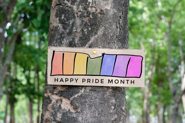 Signpost which has rainbow drawing with texts 'Happy Pride Month' sticked on tree trunk in public park to celebrate and to greet LGBT people events in pride month and to respect gender diversity.