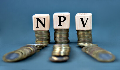 NPV - acronym on wooden cubes against the background of stacks of coins