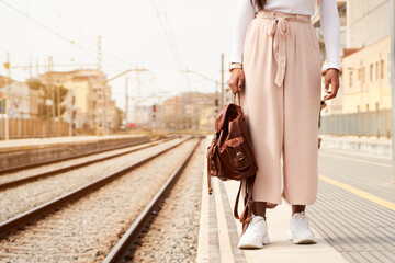 Unrecognizable female train traveler with backpack is waiting at railroad station platform. Copy space.