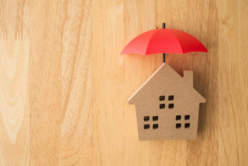 Red umbrella cover home model on wooden background copy space. House, real estate, property insurance business, mortgage loan insurance concept. Insurance is risk control management.