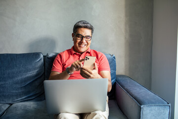 MIddle aged latin man using a smart phone on a couch at home
