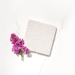 Cosmetics skin care product presentation flat lay scene and display made with pumice stone podium and lilac flowers. Studio photography. Square composition.