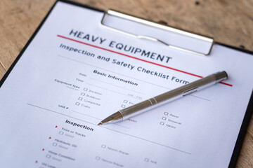 A ballpoint pen is placed on heavy equipment inspection and checklist form. Industrial safety working practive scene and object photo, close-up and selective focus at pen's part.