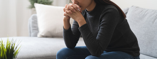 Unhappy anxiety young Asian woman sitting on the sofa at home.
