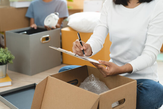 Happy woman checking stuff in cardboard box before sent to transportation company and moving to new location apartment.