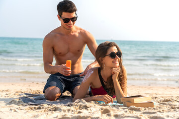 Fototapeta premium Vacation love young happy smile couple in honeymoon travel holiday trip standing on sand at blue sky sea beach applying suncream with sun drawn on tropical beach.Summer travel