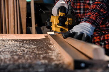 Carpenter craftsman using electric hand wood planer making pool cue or snooker cue in carpentry workplace in an old wooden shed. Handmade craftsman concept. Selective focus on wood planing.