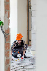 A female construction worker checks the installation of a warm floor with a tape measure at the construction site.