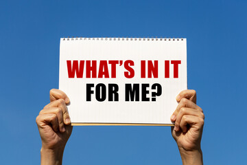 What's in it for me text on notebook paper held by 2 hands with isolated blue sky background. This...
